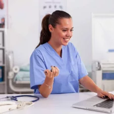 medical nurse smiling in blue scrubs in front of computer